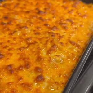 Op de afbeelding: Een close-up van een gebakken ovenschotel met macaroni en kaas. De bovenkant is goudbruin en borrelt, met een rijke, kazige textuur. De schotel bevindt zich in een donkere, rechthoekige bakvorm.