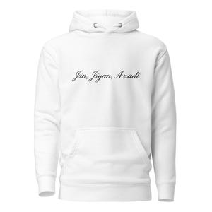May include: A white hoodie with a front pocket and a drawstring hood. The script "Jin, Jiyan, Azadi" is printed in black cursive across the chest. The hoodie is made of a soft material.