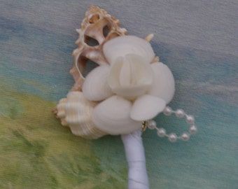 May include: A white seashell flower boutonniere with a pearl necklace accent and a white satin ribbon.