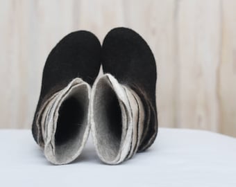 May include: A pair of black felt boots with a layered design in shades of gray and white. The boots are turned inside out, showing the layers of felt.
