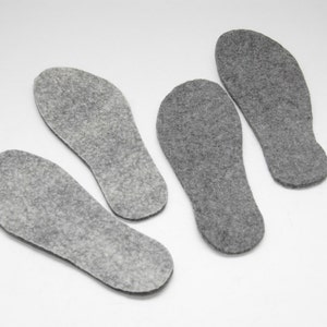 May include: Four grey felt insoles for shoes. The insoles are shaped like feet and are designed to provide comfort and support.