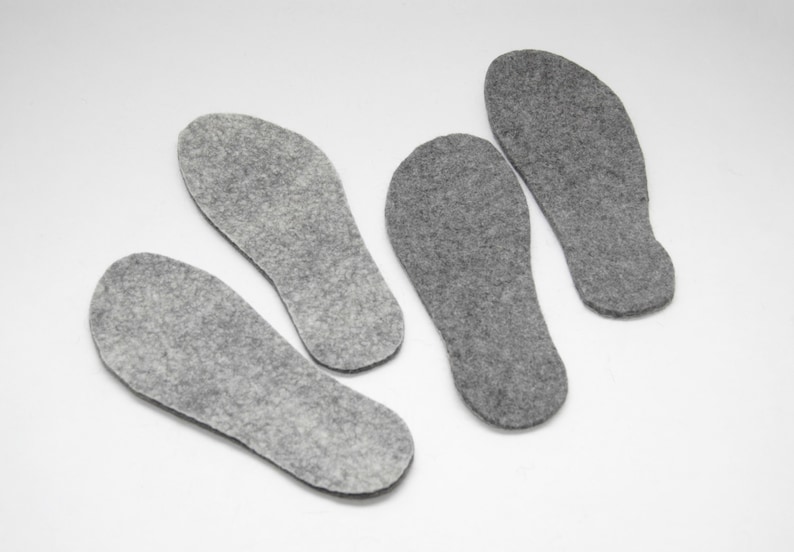 May include: Four grey felt insoles for shoes. The insoles are shaped like feet and are designed to provide comfort and support.