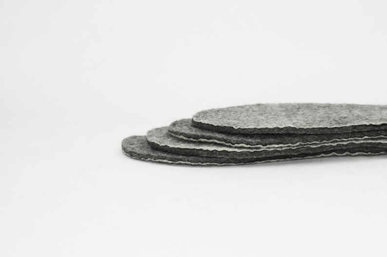 May include: A stack of five grey felt circles, each with a white edge, arranged in a graduated size.
