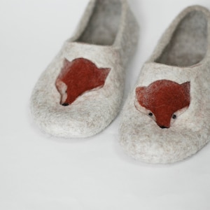 May include: A pair of gray felt slippers with a fox design on the front. The fox is made of felt and is a reddish-brown color.