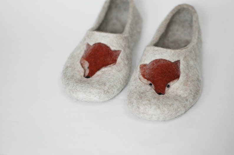 May include: A pair of gray felt slippers with a fox design on the front. The fox is made of felt and is a reddish-brown color.