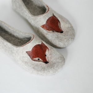 May include: A pair of gray felt slippers with a fox face embroidered on the front. The fox has a brown face and black eyes.