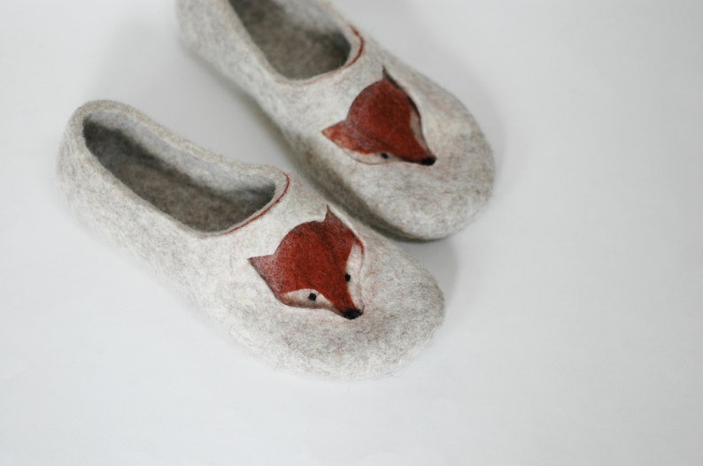 May include: A pair of gray felt slippers with a fox face embroidered on the front. The fox has a brown face and black eyes.