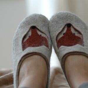 May include: A pair of gray felt slippers with a fox face design on the front. The fox face is made of brown felt and has black eyes.