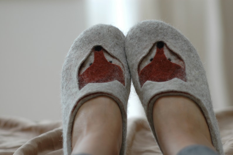 May include: A pair of gray felt slippers with a fox face design on the front. The fox face is made of brown felt and has black eyes.