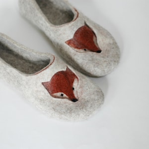 May include: A pair of gray felt slippers with a fox design. The fox is embroidered in orange and brown.