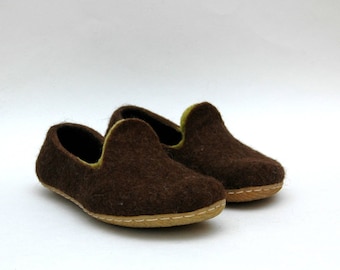 May include: A pair of brown felt slippers with a green trim. The slippers have a simple, slip-on design and a brown leather sole.