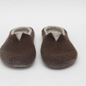 May include: A pair of brown felt slippers with a light brown lining. The slippers are closed-toe and have a rounded toe.