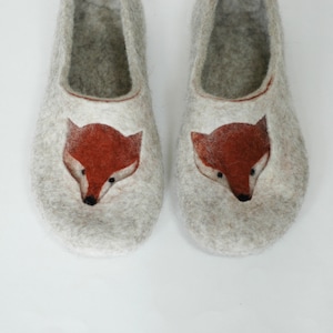 May include: A pair of gray felt slippers with a fox face design. The fox faces are embroidered in orange and brown.