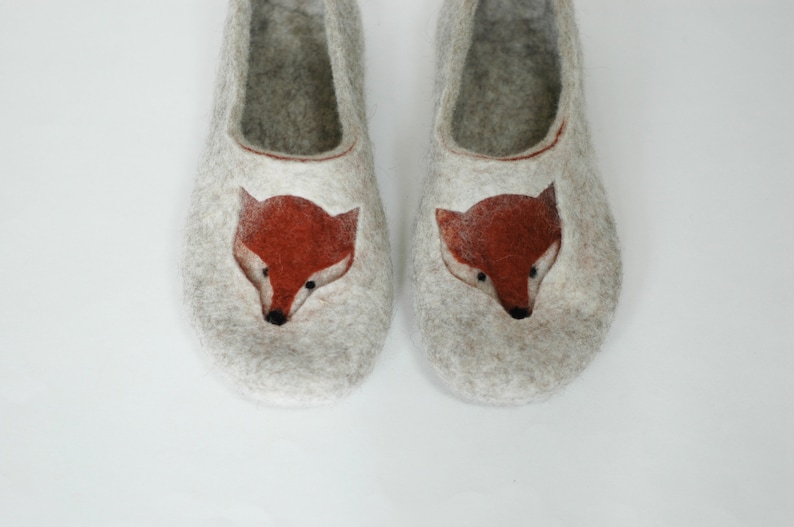 May include: A pair of gray felt slippers with a fox face design. The fox faces are embroidered in orange and brown.