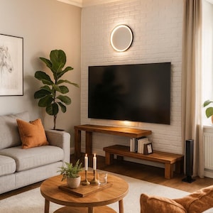 Puede incluir: Salón moderno con sofá gris, cojín naranja y mesa de centro de madera. Un televisor de pantalla plana grande está montado en una pared de ladrillo blanco sobre una consola de madera. Una lámpara decorativa y una planta en maceta.