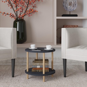May include: A small, two-tiered side table with a dark blue top and bottom and natural wood legs. Two white teacups sit on the top tier, along with a black phone. A stack of books is on the lower tier. The table is between two white armchairs.