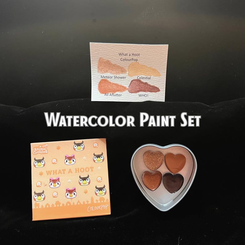May include: A watercolor paint set with the text "WATERCOLOR PAINT SET". The set includes a square box with owl graphics and the text "WHAT A HOOT". A heart-shaped palette contains four eyeshadows. A swatch card displays eyeshadow colors.