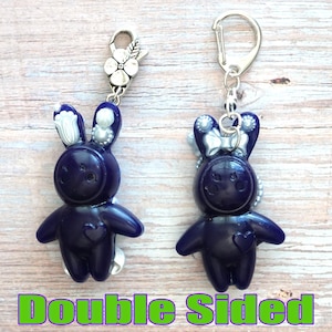 May include: Double-sided charm featuring a dark blue bunny with silver accents and a heart on its chest. The charm is attached to a silver key ring with a flower-shaped clasp.
