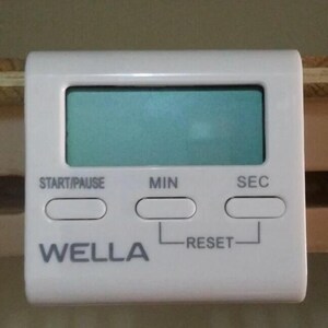 Pode incluir: Um temporizador de cozinha digital branco com um visor retangular e tr&ecirc;s bot&otilde;es rotulados como "START/PAUSE", "MIN" e "SEC". A marca "WELLA" est&aacute; impressa na frente. O temporizador tem um bot&atilde;o "RESET".