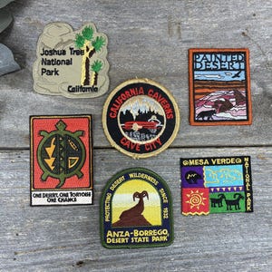 May include: Six embroidered patches featuring national and state park themes. Designs include Joshua Tree National Park, California Caverns, Painted Desert, a tortoise with the text One Desert, One Tortoise, One Chance, Anza-Borrego, and Mesa Verde.