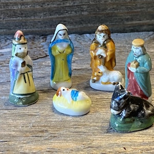 May include: A collection of small, hand-painted ceramic nativity figurines. The set includes figures of Mary, Joseph, the baby Jesus, the three wise men, a shepherd, and a donkey. The figurines are painted in bright colors and have a glossy finish.