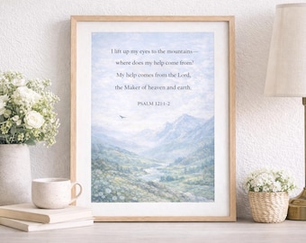 May include: Framed art print featuring a serene mountain landscape in shades of blue and green. The print includes the text of Psalm 121:1-2 in a simple font. The artwork is displayed on a table with a vase of white flowers, a mug, and a stack of books.