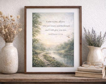 May include: Framed landscape art print with a serene river scene, trees, and a path. The artwork features the text "Come to me, all you who are weary and burdened, and I will give you rest. Matthew 11:28". The print is displayed on a wooden surface.