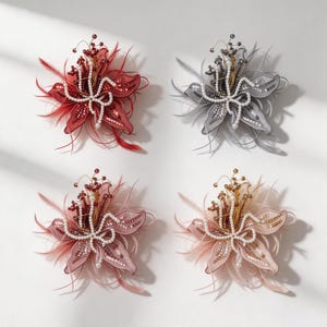 May include: Four floral brooches in red, gray, dusty rose, and champagne. Each brooch features fabric petals adorned with sequins, delicate feathers, and a central cluster of white faux pearls and metallic beads on thin, flexible wire stems.