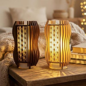 Può includere: Due lampade in legno con una calda luce. Le lampade hanno un design unico con doghe di legno verticali e un motivo geometrico al centro. Sono su un tavolo di legno, creando un'atmosfera accogliente e invitante.