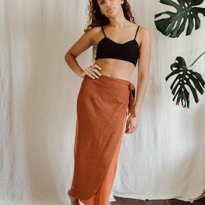 Puede incluir: Un top corto negro y una falda envolvente en tonos naranja y marrón. La falda está atada a la cintura y tiene un diseño fluido. El atuendo es informal y adecuado para climas cálidos.