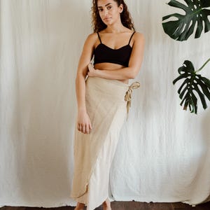 Puede incluir: Un top negro de tirantes finos y una falda envolvente beige. La falda se ata a la cintura con una cinta de tela a juego. El conjunto es sencillo y elegante, adecuado para el clima cálido o una ocasión informal.