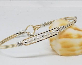 May include: A gold and silver wire wrapped bangle bracelet with a row of white pearls and silver beads.