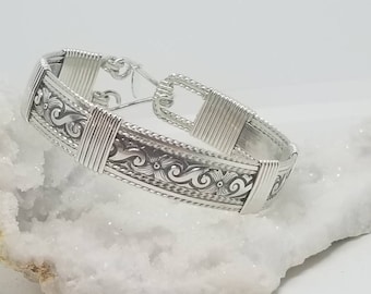 Könnte beinhalten: Ein silbernes Armband mit floralem Muster. Das Armband ist aus Draht gefertigt und hat einen Verschluss.