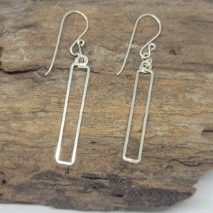 May include: A pair of silver dangle earrings with a simple rectangular design. The earrings have a hook closure.
