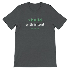 May include: Dark grey t-shirt featuring the text ">build with intent" in white and green. The shirt has a crew neck and short sleeves. Three green dots are below the text.