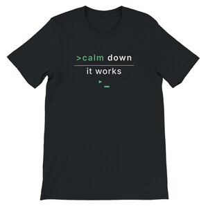 May include: Black t-shirt featuring the text ">calm down it works" in white and green. The design is minimalist, with the text in a clear font. The t-shirt has a crew neck and short sleeves, suitable for casual wear.