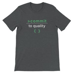 Può includere: T-shirt grigio scuro con la scritta ">commit to quality" in verde e bianco. La maglietta ha girocollo e maniche corte. Il testo è centrato sul davanti della maglietta.