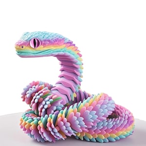 Puede incluir: Un juguete de serpiente articulada y colorida en tonos pastel. La cabeza de la serpiente es azul claro con ojos rosas, y su cuerpo en tonos de rosa, amarillo y verde. El juguete está diseñado para ser flexible y posable, enrollado en un patrón circular.