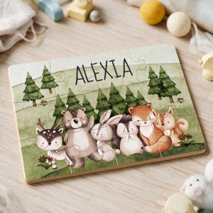 Könnte beinhalten: Ein rechteckiges Holzpuzzle mit einer Waldszene, die einen Hirsch, einen Bären, einen Hasen, einen Igel, einen Fuchs und ein Eichhörnchen zeigt. Der Name ALEXIA ist oben in schwarzen Großbuchstaben aufgedruckt. Der Hintergrund zeigt grüne Hügel.