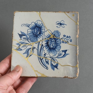 May include: A blue and white ceramic tile with a floral design. The tile is cracked and has gold accents.
