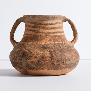 May include: A rustic, earthenware vessel with two handles. The pot features a rounded body and a cylindrical neck. The exterior is a mottled brown with horizontal bands of darker brown near the top. This antique-style pottery is suitable for home decor.