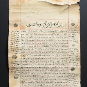 May include: An old, yellowed, and faded document with Arabic text written in black ink. The document is rolled up and has a red seal at the top. The text includes the phrase "Bismillah al-Rahman al-Rahim" which translates to "In the name of Allah, the Most Gracious, the Most Merciful."