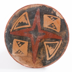 May include: A round, earthenware bowl with a dark brown interior and a reddish-brown starburst design. The bowl features geometric shapes in tan and black, with a light brown exterior.