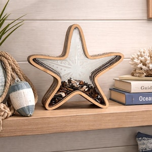 May include: A wooden starfish-shaped decorative piece with a clear glass center filled with shells and small stones. The starfish sits on a wooden shelf with other coastal decor, including a potted plant, rope, and books.