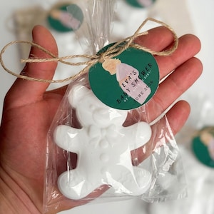 May include: A white teddy bear-shaped soap in a clear cellophane bag, tied with twine and a green tag. The tag reads "EVA'S BABY SHOWER" and "JUNE 2026". The soap is a baby shower favor.