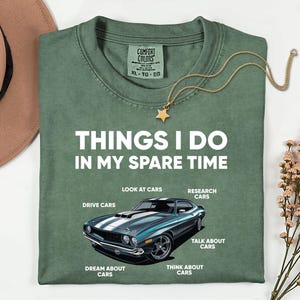 Könnte beinhalten: Grünes T-Shirt mit dem Text "THINGS I DO IN MY SPARE TIME" und einer Grafik eines türkisblauen Autos. Das Shirt listet auch "LOOK AT CARS", "DRIVE CARS", "DREAM ABOUT CARS", "RESEARCH CARS", "TALK ABOUT CARS" und "THINK ABOUT CARS" auf. Eine goldene Sternkette liegt auf dem Shirt.