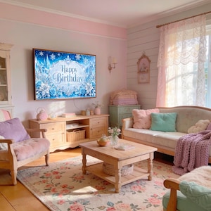 May include: A cozy living room with a floral rug, wooden furniture, and a TV displaying "Happy Birthday." The room features a sofa with pastel pillows and a chunky knit throw, creating a soft, inviting atmosphere. A cabinet and armchair add to the room's charm.