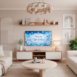 May include: A living room scene with a light color palette. A TV displays a "Happy Birthday" message with blue and white floral and snowflake accents. The room features two white sofas, a round coffee table, and a wooden entertainment center.