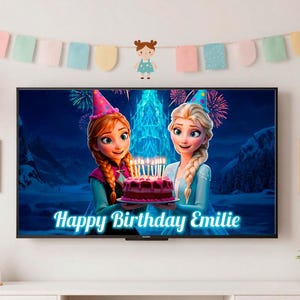 May include: A television screen shows a birthday scene with animated characters holding a cake with lit candles. The text "Happy Birthday Emilie" is displayed on the screen. The room is decorated with balloons, a banner, and framed artwork.