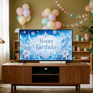 May include: A modern living room with a wooden TV stand, a large screen displaying "Happy Birthday" with blue floral and snowflake designs. Balloons and a giraffe plush toy add to the festive atmosphere. A potted plant is on the right.